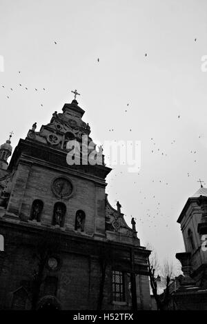 Une vieille église et une volée de corbeaux sur le fond du ciel en noir et blanc de Lviv. Banque D'Images