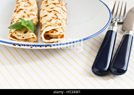 Crêpes crêpes minces laminées menthe sur une plaque avec couteau et fourchette. Banque D'Images