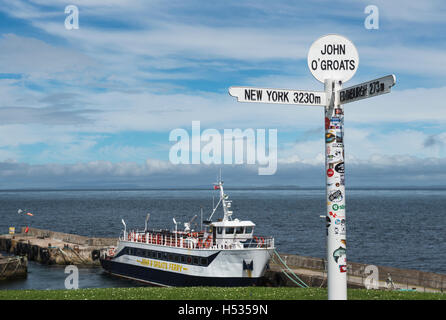 Le célèbre panneau multi-directionnel à John O'Groats à Caithness, Ecosse, avec le John O'Groats ferry dans l'arrière-plan Banque D'Images