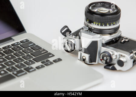 Appareil photo vintage et un ordinateur portable sur un tableau blanc avec fond blanc. appareil photo avec un objectif 50 mm située à l'envers Banque D'Images