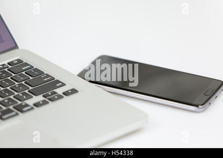 Smartphone et laptop lying côte à côte sur une table.. les deux désactivés. studio shot sur un fond blanc Banque D'Images