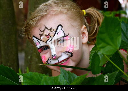 Une jeune fille se profile derrière l'épais feuillage vert avec un sourire espiègle et lumineux face à la peinture. Banque D'Images