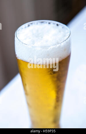 Tête de mousse sur un verre de bière sur fond blanc et noir en diagonale Banque D'Images