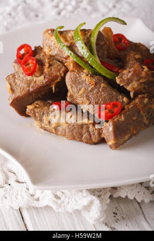 Boeuf Rendang mijotée dans le lait de coco aux épices gros plan sur une plaque verticale sur la table. Banque D'Images