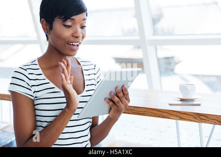 Happy afro-américain businesswoman holding tablet computer and waving in office Banque D'Images