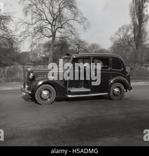 Années 1950, tableau historique d'un taxi noir de Londres 3 portes sur la route, avec sa plate-forme ou un compartiment bagages ouvert à côté du conducteur. Banque D'Images