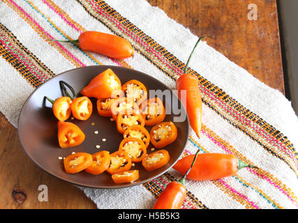 Assiette de piment orange avec joints toriques et les graines des piments entiers sur table avec tapis coloré Banque D'Images