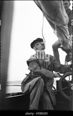 Une jeune femme est photographiée dirigeant un yacht à la voile, mettant en valeur à la fois ses compétences de voile et la beauté classique du yachting. La photo capture un moment d'activité nautique et de réalisation personnelle. Banque D'Images