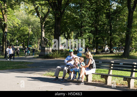 La famille, les parents et deux enfants, assis sur un banc et de manger des glaces - profiter du temps ensemble sur une journée ensoleillée dans un parc Banque D'Images