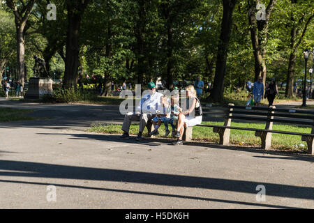 La famille, les parents et deux enfants, assis sur un banc et de manger des glaces - profiter du temps ensemble sur une journée ensoleillée dans un parc Banque D'Images