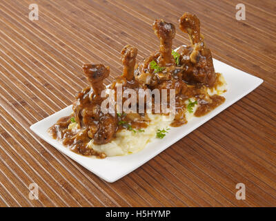 Morceaux de sucette de poulet placés sur une purée de pommes de terre bouillies et garnis de sauce tomate-ail dans un plat Banque D'Images