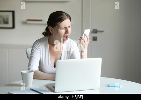 Portrait d'une femme au bureau avec ordinateur portable, à la recherche au mobile Banque D'Images