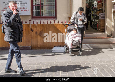 Un homme debout avec un bébé dans un landau. Un passant est de fumer une cigarette pendant qu'il marche par à Chinatown, Soho, Londres. Banque D'Images