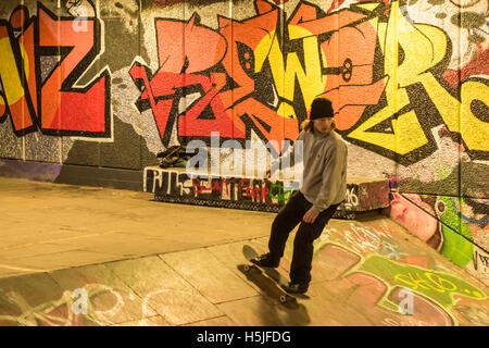 Un skateur professionnel dans un passage souterrain dans le quartier londonien de South Bank. Le mur derrière lui est couvert de graffitis colorés et éclairée de néons. Banque D'Images