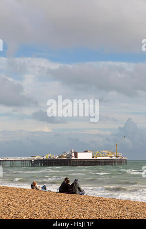 Des gens assis sur la plage de Brighton à Brighton Pier en automne, Brighton, East Sussex England UK Banque D'Images