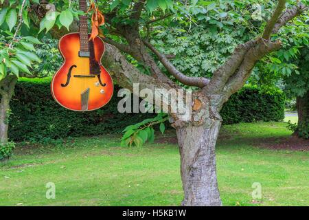 Rouge et jaune une guitare acoustique Hofner suspendu à des branches d'arbre dans un parc Banque D'Images