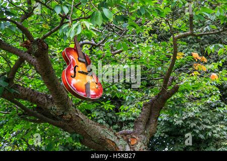 Rouge et jaune une guitare acoustique Hofner suspendu à des branches d'arbre dans un parc Banque D'Images