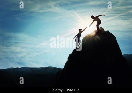 Silhouette de coup de main entre deux garçons l'ascension d'une falaise rocheuse dangereuse. Amicalement la main sur la haute montagne randonnée. Inspirati Banque D'Images