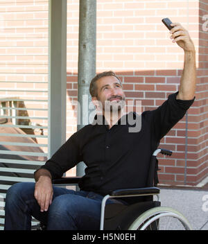 Bel homme en fauteuil roulant en prenant un sourire et selfies Banque D'Images