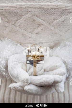 Close-up of woman's hands en gants blancs tenant une petite boîte cadeau de Noël d'argent Banque D'Images