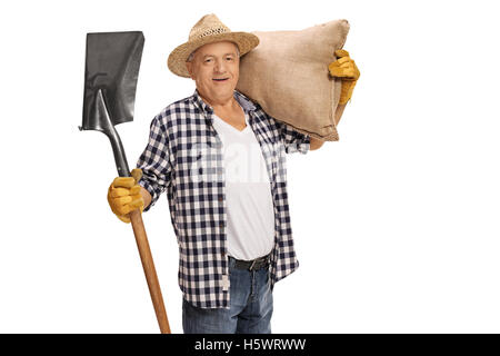 Fermier âgé joyeux posant avec une pelle et un sac de jute isolé sur fond blanc Banque D'Images