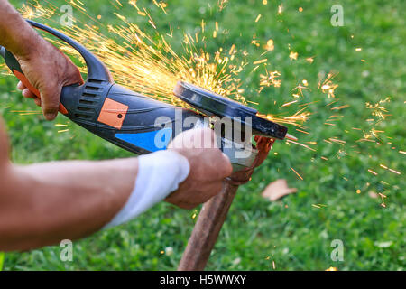 Les mains du travailleur blessé couper le métal avec une meuleuse. Tandis que le broyage de Sparks Banque D'Images