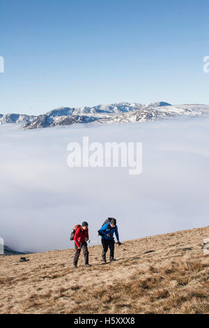 Deux alpinistes grimper hors d'une inversion de température en hiver soleil sur les pentes du grand Rigg, vedette de Fairfield. Banque D'Images