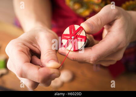 Bouilloire bouton en troisième étape de production d'Posamentenknöpfe avec vierge en bois holding vice et soigneusement wrapping fil rouge Banque D'Images