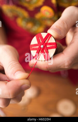 Bouilloire bouton en troisième étape de production d'Posamentenknöpfe avec vierge en bois holding vice et soigneusement rétractable en fil rouge Banque D'Images