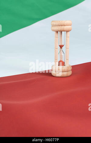Sablier en bois contre un drapeau italien - une métaphore visuelle pour le temps presse pour les banques et le système financier italien  + crise de la dette souveraine. Banque D'Images