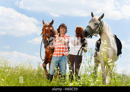 Couple aimant la marche avec les chevaux dans le champ d'été Banque D'Images