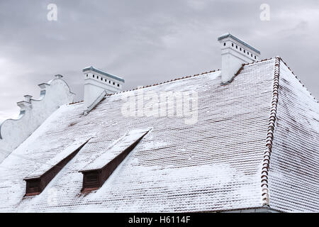 Toit de tuiles de vieille maison avec lucarnes et cheminées sous la neige Banque D'Images