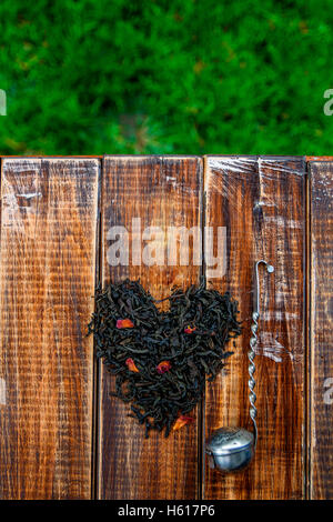 Crépine Vintage près de feuilles sèches de thé noir faites en coeur sur table en bois dans le jardin et sur la nature. Concept de thé. Plateau Banque D'Images