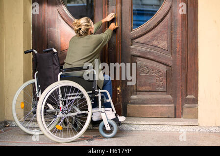 Femme en fauteuil roulant en face de porte d'entrée que vous essayez de tomber dans Banque D'Images