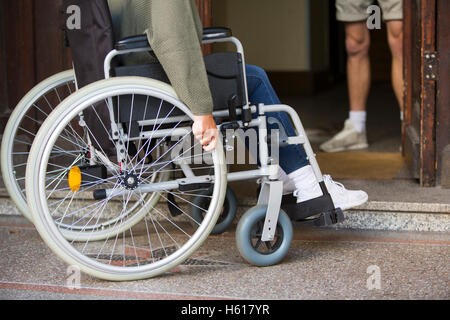 De gros plan femme en fauteuil roulant devant une porte d'entrée Banque D'Images