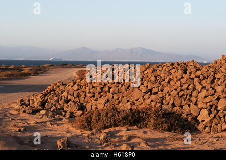 Fuerteventura, Îles Canaries, l'Afrique du Nord : un mur de pierre et vue sur le profil de Lanzarote au coucher du soleil sur le chemin de terre Majanicho à Corralejo Banque D'Images