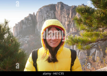 A smiling chinese woman portant des lunettes et un manteau d'hiver jaune tôt le matin sur le Mont Taishan ou Tai dans le Shandong. Banque D'Images