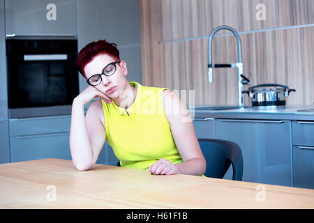 Femme en robe jaune assis à table de cuisine et chambre Banque D'Images