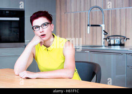 Femme en robe jaune assis à table de cuisine à la colère Banque D'Images