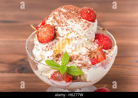 Délicieux dessert rose boules de glace avec des fraises fraîches, saupoudrées de chocolat et menthe dans un bol sur fond de bois, Banque D'Images