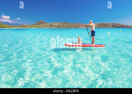 Père heureux avec son petit fils s'amusant sur le stand up paddle board sur l'île de Corse, France. Banque D'Images