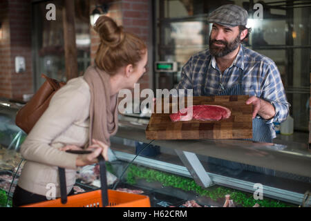 Butcher montrant la viande pour femme en boucherie Banque D'Images