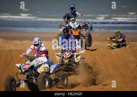 Margate, Kent, Royaume-Uni. 22 octobre 2016. Quatre pilotes de véhicules tout-terrain s'affrontent sur une plage de sable, dégageant la poussière en naviguant sur les dunes et les terrains accidentés. Un VTT est en vol, capturant le frisson et l'intensité de la course hors route. Les coureurs portent des casques et des combinaisons de course, avec des plaques d'immatriculation visibles suggérant une compétition. L'océan et les spectateurs lointains encadrent le cadre côtier dynamique. Cromwell Truck Sales/Ovendens BXUK Margate International Beach Cross. Crédit : Penelope Barritt/Alamy Live News Banque D'Images