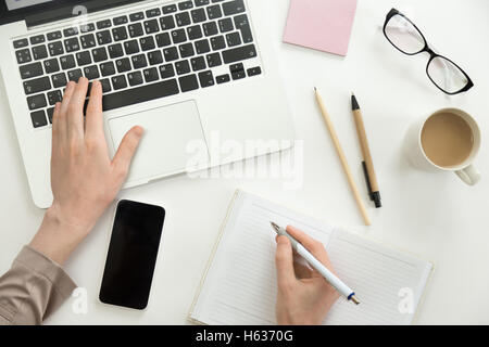 La main travaillant sur un ordinateur portable, l'autre tenant un stylo Banque D'Images