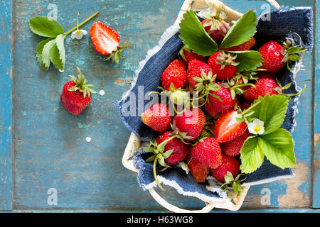 La récolte des fraises mûres fraîches dans un panier en osier sur la vieille table en bois, vue du dessus. Banque D'Images