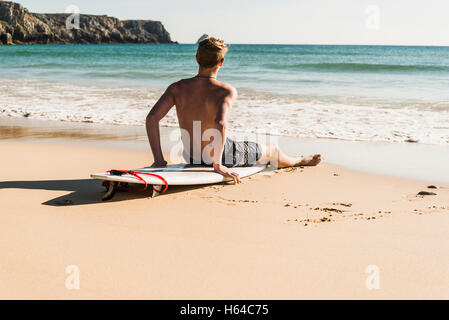 Teenage boy sitting on surfboard à la mer Banque D'Images