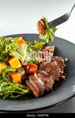 Salade avec du potiron, de la viande grillée et salade verte fraîche de canard sur une assiette et une fourchette avec la salade dans l'air Banque D'Images