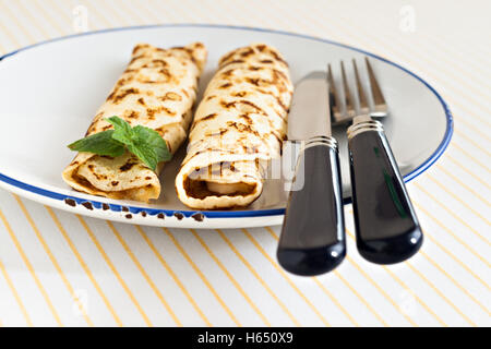 Crêpes crêpes minces laminées menthe sur une plaque avec couteau et fourchette. Banque D'Images