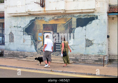 Couple walking passé effet Trompe l'oeil Peinture Peinture murale sur le côté d'un immeuble dans la ville de Swanage, Dorset, Angleterre. Banque D'Images