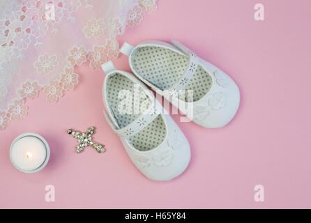 Paire de chaussons pour bébé blanc sur fond rose avec dentelle robe de baptême et la bougie Banque D'Images